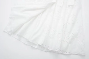 Detail view of the intricate eyelet embroidery and wavy hem on a white midi dress