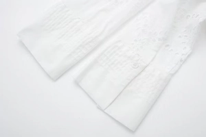 Detailed macro view of white sleeve cuffs featuring eyelet embroidery and pin-tuck pleats
