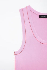 Detail of pink knitted vest featuring red contrast stitching and refined seam textures