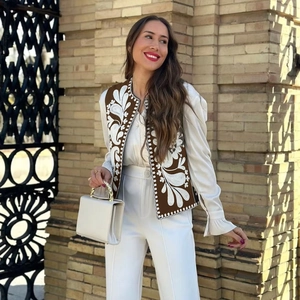 Détail d'un gilet marron avec broderie florale blanche et sac à main à chaîne dorée