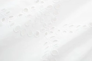Detail of white Broderie Anglaise midi dress showing intricate floral embroidery texture