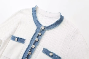 Details von weißer Strickjacke mit blauem Denim-Besatz und silbernen Reliefknöpfen