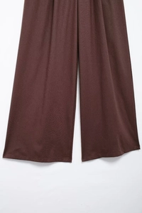 Gros plan détaillé montrant la coupe ample et le drapé du pantalon large en lin marron