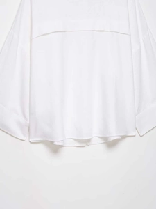 Detail of loose batwing sleeves and curved hem on a minimalist white cotton shirt