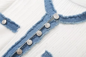Makro-Detail des weißen Rippstricks mit Denim-Besatz und silbernen Ankerknöpfen