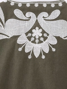 Gros plan d'une broderie florale blanche sur tissu de coton-lin vert olive foncé