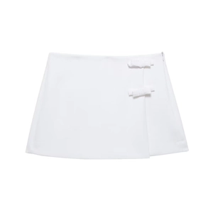 Détail d'une mini-jupe blanche trapèze avec nœuds décoratifs et fermeture éclair latérale