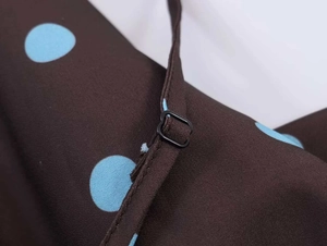 Detail of adjustable black shoulder strap buckle on brown blue polka dot camisole