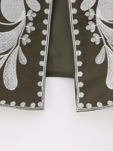 Gros plan sur la broderie florale blanche d'un gilet sans manches vert foncé en toile