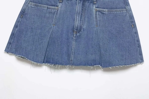 Detail view of denim mini skirt featuring raw hem edge and pleated texture design