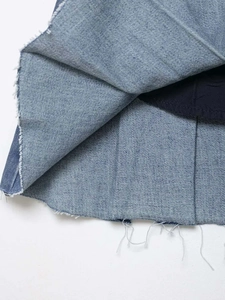 Detail view of light blue washed denim skirt showing pleats and frayed hemline with lining
