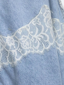 Close-up of light blue washed denim jacket with white floral eyelash lace trim details
