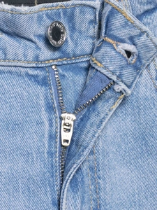 Vue macro détaillée de la fermeture éclair YKK et du bouton gravé sur un jean bleu