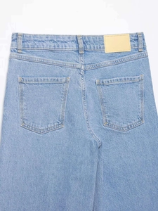 Détail de jean taille haute bleu clair montrant les poches arrière et le patch en cuir