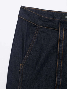 Detailed close-up of dark blue denim fabric with contrast orange stitching and waistband