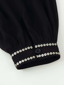 Close-up of black blouse cuff with silver sequins and a single button closure
