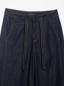 Detail of high waist dark blue denim trousers with tie belt and contrast orange stitching