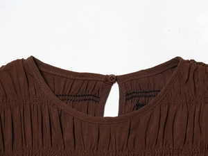 Detail of round neckline with pleats, black stitching, and back button on brown dress