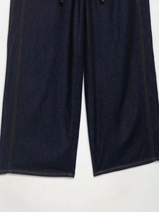 Detail of dark blue denim trousers featuring orange contrast stitching and straight wide legs