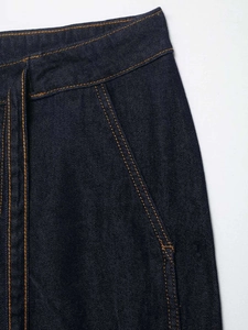 Detailed macro view of dark indigo denim fabric with contrasting orange double stitching