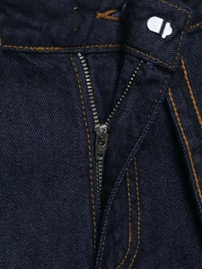 Detailed macro view of dark blue denim jeans featuring a metal YKK zipper and orange stitching