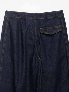 Detail of dark blue denim jeans showing contrast orange stitching and flap back pocket