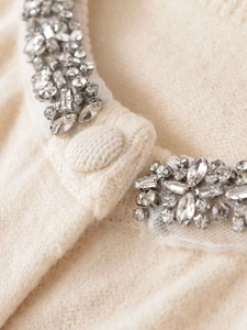 Detailed close-up of rhinestone and sequin embellishments on a beige knit cardigan neckline