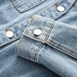 Close-up of light blue denim dress with V-neck, metal buttons and orange stitching