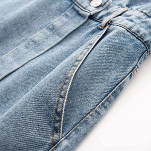 Close-up of light blue denim dress showing waist pleats, metal button and fabric texture