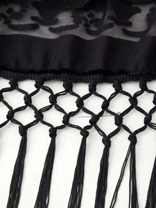 Detail von schwarzem floralem Spitzenstoff mit gewebtem Netz und langen Fransen-Details