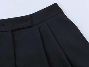 Detailed view of black high-waisted pleated trousers with precise stitching and fabric texture