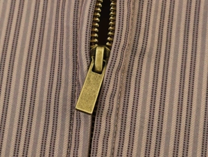 Detail of vintage bronze metal zipper on pinstriped blazer fabric with macro focus