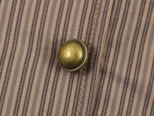 Macro detail of retro bronze metal button on striped tailored blazer fabric