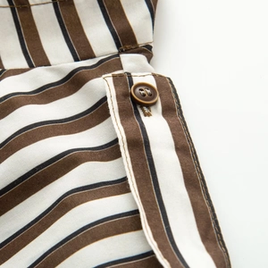 Détail d'une veste rayée montrant un bouton marron et des finitions de couture fines
