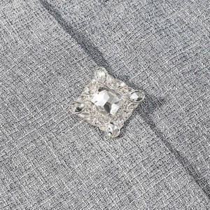 Elegant square crystal brooch featuring a large center stone on gray suit fabric