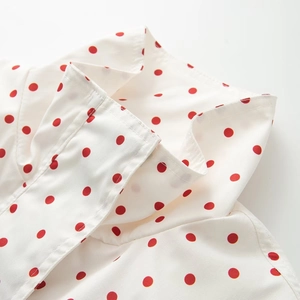 Close-up detail of stand-up collar with red polka dots on white woven fabric top