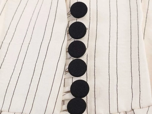 Close-up of vertical black fabric-covered buttons on beige striped blazer jacket