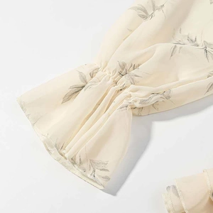 Detail of ruffled elastic cuffs on a cream-colored chiffon dress with leaf prints