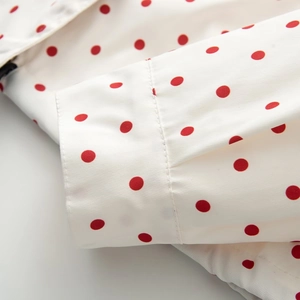 Detailed close-up of double stitching and red polka dot print on white sleeve cuff
