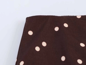 Detailed view of dark brown high-waisted wide leg trousers with pink polka dot print