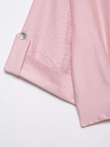 Close-up of pink blouse sleeve with pearlescent button detail and textured fabric