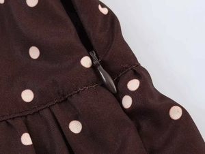 Detail of invisible zipper closure on dark brown polka dot high-waisted trousers