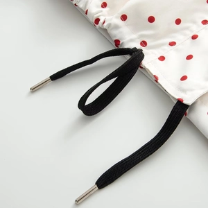 Detail of white fabric with red polka dots and black woven drawstring with metal aglets