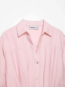 Close-up of the V-neck collar and silver metal button on a light pink textured shirt