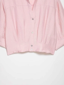 Detail of pink satin V-neck blouse showing textured fabric, buttons, and pleated waist