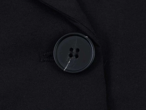 Detailed close-up of a four-hole black button on a textured twill woven fabric blazer