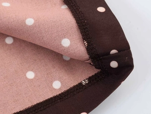 Close-up of pink polka dot fabric with high-quality brown hem stitching and soft texture