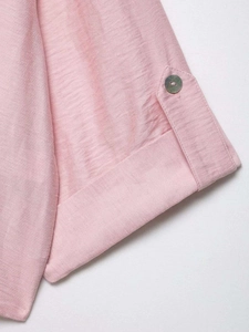 Detail of pink cotton shirt sleeve featuring adjustable rolled cuff and bronze button tab