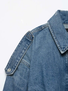 Detail of blue denim jacket shoulder with metallic silver buttons and epaulettes