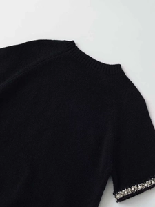 Dettaglio maglione nero a maniche corte in maglia con decorazioni di perle e strass sui polsini